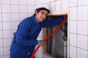 Electrician feeding red pipe behind a tiled wall