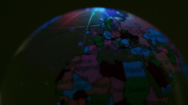 Toy Earth sphere with world map on it spins in color light
