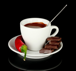 white cup with hot chocolate and chili pepper isolated on black