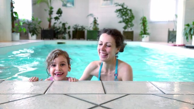 Little girl with her mother stay on edge of indoor pool