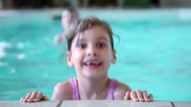 girl jumps in water near edge of pool, brother at background