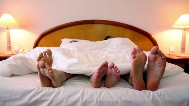 Parents with their son lay in bed and move bootless feet
