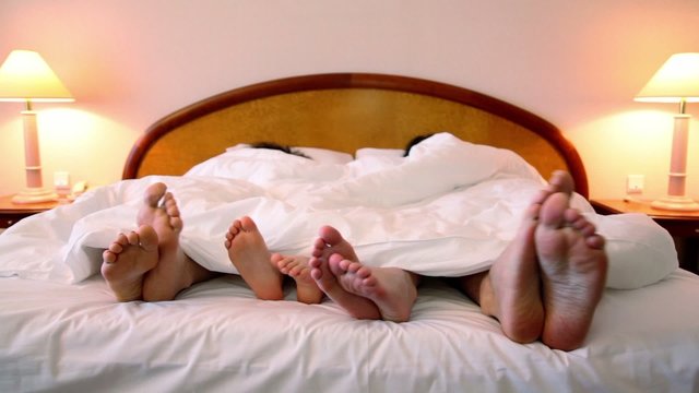 Family lay in bed under blanket and move bootless feet