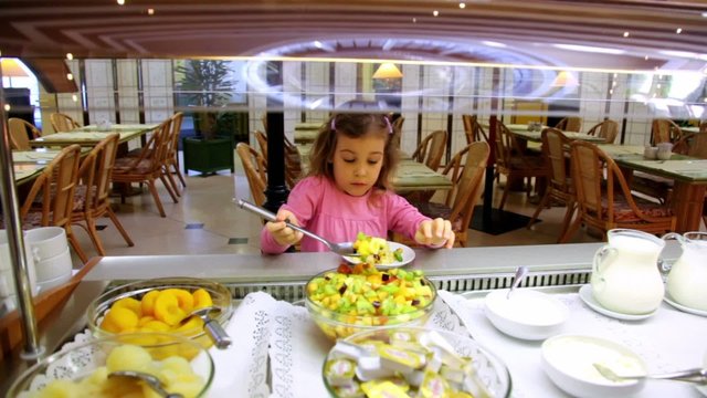 Little girl takes food and put it on plate at breakfast time