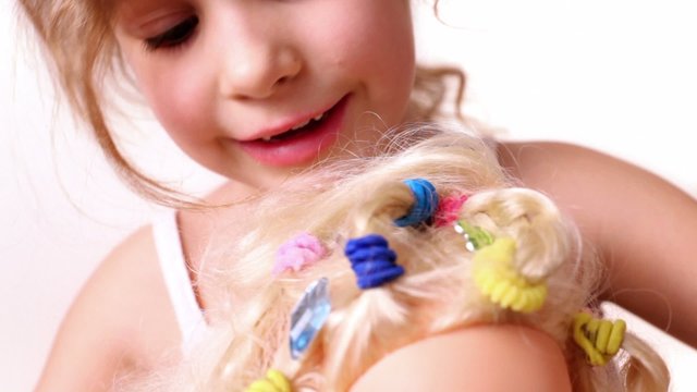 Little girl decorate dolls hairdo with bijouterie crystal