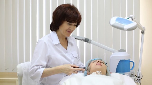 Beautician does galvanotherapy on face to client