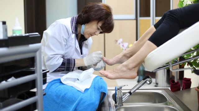 Cosmetician does pedicure to woman and has spread on towel