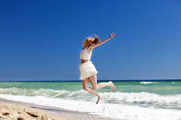 Young redhead girl jumping at the beach.