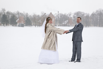 Fototapeta na wymiar Newly married holding hands on freezing lake area in winter 