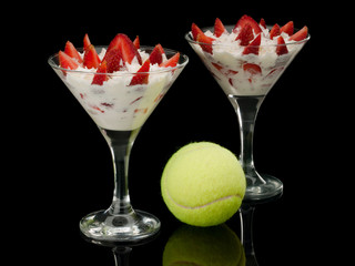 Tennis ball and strawberry with cream in two glasses.