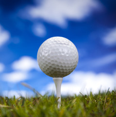 Golf ball on green grass over a blue sky 