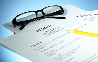 Closeup of resume with glasses and pencil on blue background