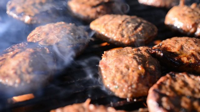hamburgers cooking on a barbeque grill with flames and smoke