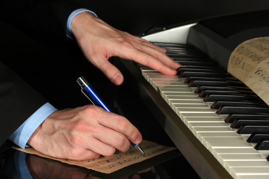 man hands playing piano and writes on parer for notes