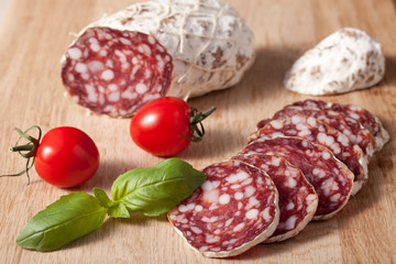 Traditional sliced salami on wooden board with basilic, cherry t