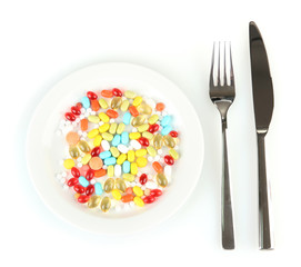 a lot of pills in a plate with knife and fork isolated on white