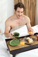 Young man having breakfast in bed