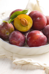Fresh wet plums with leaves in the bowl on the vintage board
