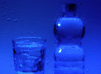 Blurred glass and bottle of water with waterdrops