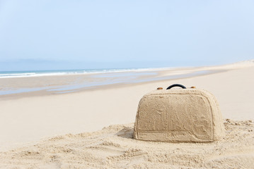 Suitcase made out of sand on beach