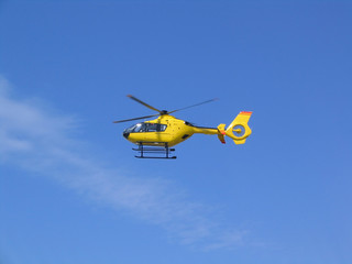 Small yellow helicopter in the air, blue sky in background