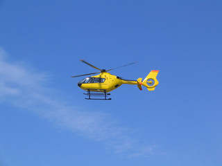 Fototapeta premium Small yellow helicopter in the air, blue sky in background