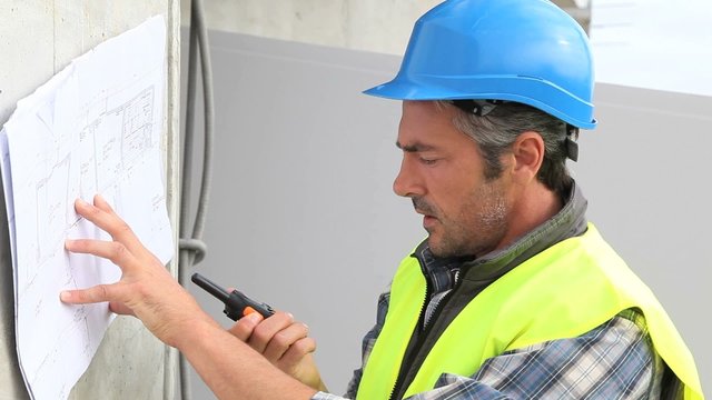 Construction manager reading plan and using walkie-talkie