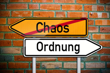 Fototapeta na wymiar Wegweiser auf Ziegelsteinwand mit Chaos und Ordnung
