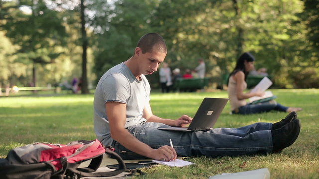 Young student with laptop relaxing in the park, steadicam shot