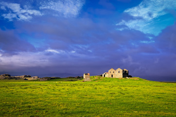 Old rusty house and barn in the green meadow and stormy clouds