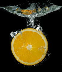 Fotobehang Schijfje sinaasappel in het water op zwarte achtergrond © Africa Studio