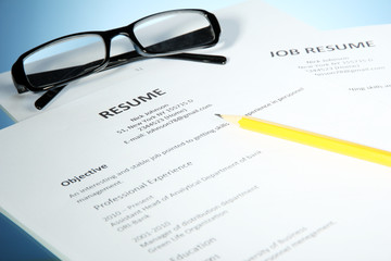 Closeup of resume with glasses and pencil on blue background