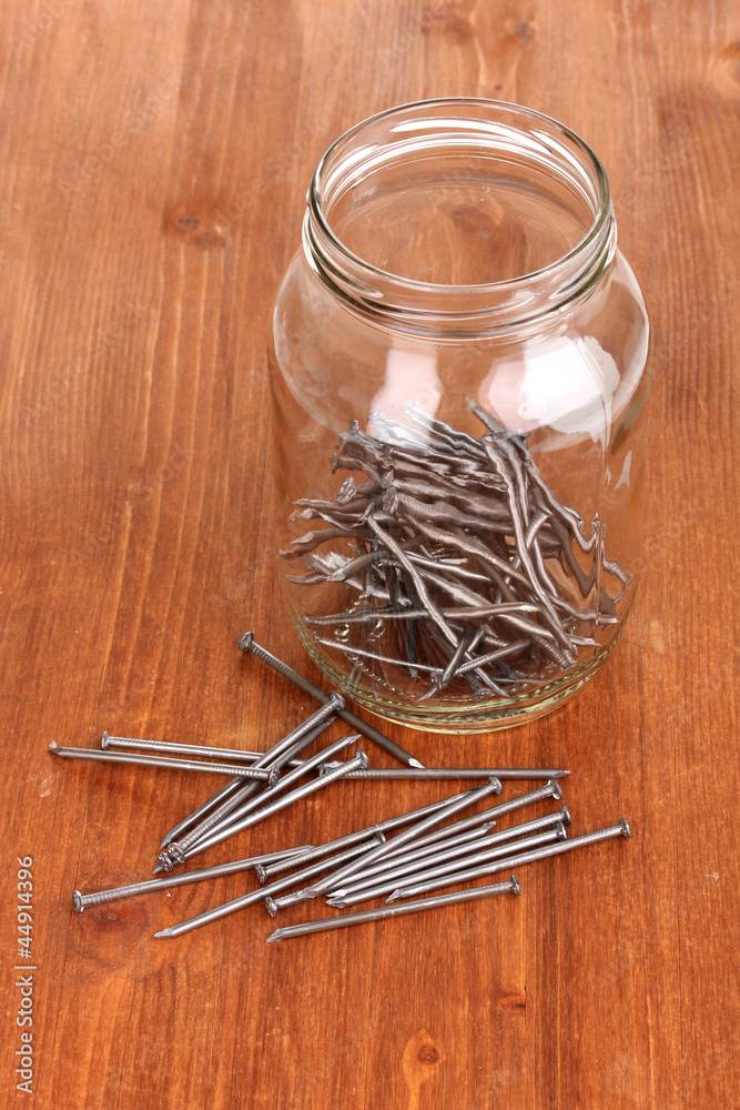 Wall mural Metal nails and glass jar on wooden background