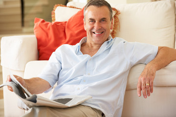 Obraz premium Senior Man Relaxing On Sofa At Home Reading Newspaper