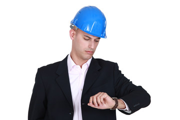 Suited man in a hardhat looking at his watch