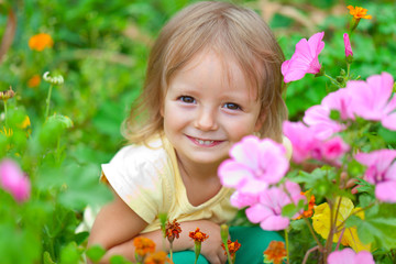 Cute little girl sitting among the flowers. Sunny summer day