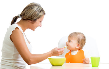 young mother spoon feeding her cute baby girl isolated on white