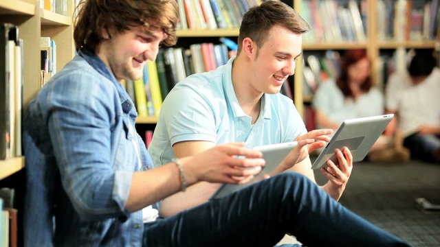 Male classmates social networking on tablets in library
