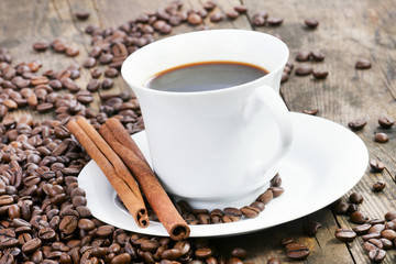 A cup of coffee, and cinnamon, coffee beans around it.