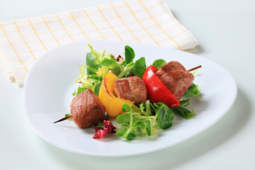 Grilled pork skewer with salad greens