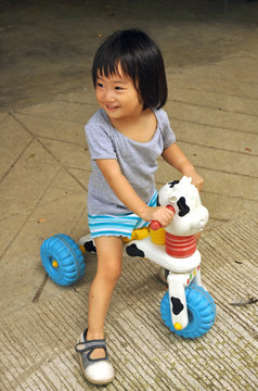 Asain Little Child Girl Is Playing On Toy With Wheels Outdoors