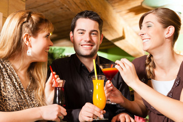 Young people drinking cocktails in bar or restaurant