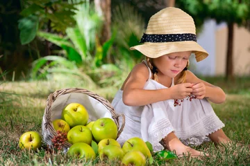 Tuinposter Девочка сидит на траве с корзиной яблой © verevs