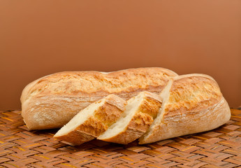 two baguette bread on a wicker table cloth on a brown background