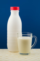 a bottle of milk with a cup on a blue background and a wicker ta