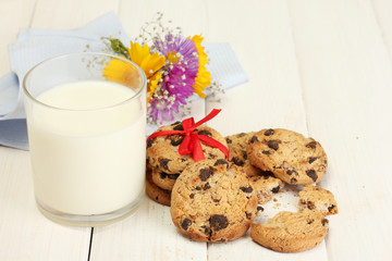 glass of milk, chocolate chips cookies with red ribbon and