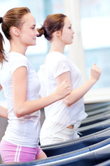 Fototapeta premium Two young sporty women run on machine