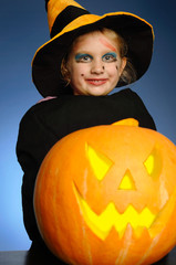 Young girl as a witch with a pumpkin on Halloween.