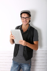 Trendy guy using electronic tablet leaning on wall