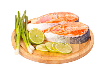Two raw salmon steaks with lime and green onion on the cutting b